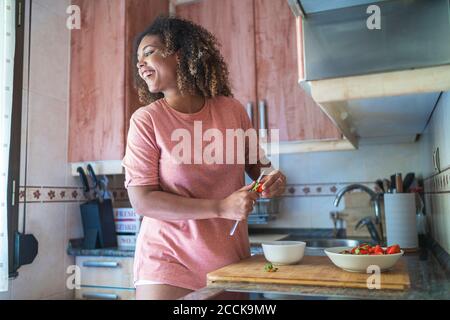 Fröhliche junge Frau, die wegschaut, während sie Erdbeeren in der Küche hackt Zähler zu Hause Stockfoto