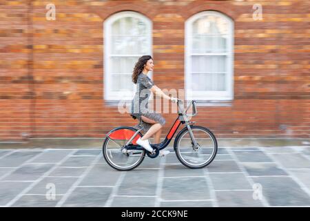 Verschwommene Bewegung der jungen Frau, die Fahrrad auf der Straße durch Gebäude in der Stadt Stockfoto
