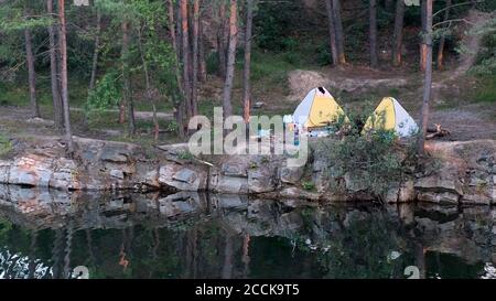 Schöne Landschaft, Camping und Zelte unter dem Pinienwald am Rande des überfluteten Granitsteinbruchs Stockfoto