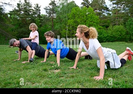 Mädchen sitzt auf Vater zurück Ausübung mit Familie über grasig Land im Wald Stockfoto