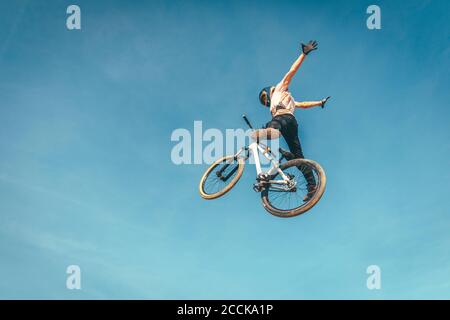 Sorgloser Mann mit Fahrrad gegen blauen Himmel während Stunt durchführen Sonnenuntergang Stockfoto