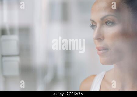 Nahaufnahme einer nachdenklichen schönen Frau, die durch das Fenster zu Hause gesehen wird Stockfoto