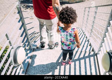 Vater hält die Hände der kleinen Tochter, während er auf Stufen steht Stockfoto