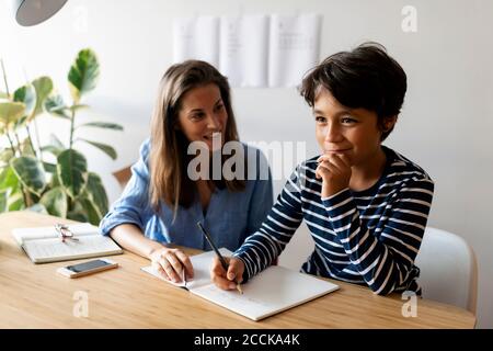 Weibliche Tutor Jungen beim Schreiben Hausaufgaben zu Hause helfen Stockfoto