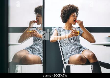 Frau, die Erdbeere aß, während sie auf dem Stuhl auf dem Balkon saß Penthouse Stockfoto