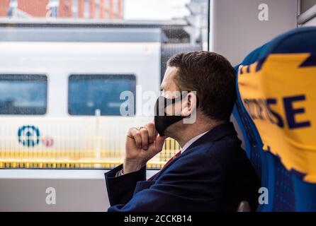 Ein Mann mit Anzug und schwarzem Gesichtsbedeckung blickt aus einem statischen Zugfenster in Leeds Bahnhof. Stockfoto