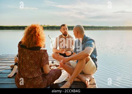 Freunde, die auf dem Steg an einem See picknicken Stockfoto