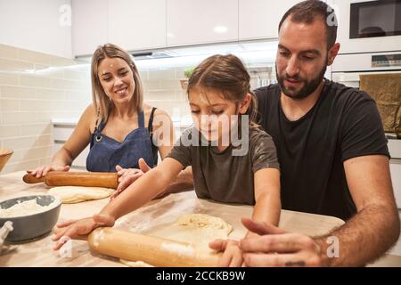 Familie Kneten Pizzateig mit Rollnadeln auf Tisch in Küche Stockfoto