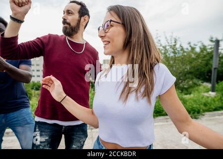 Glückliche Freunde, die wegschauen, während sie im Park gegen den Himmel tanzen Stockfoto