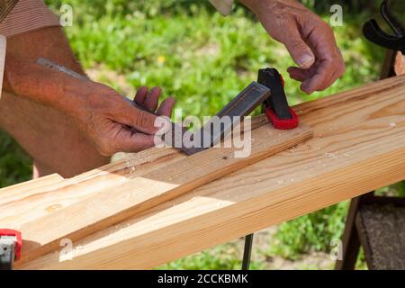 Nahaufnahme von erwachsenen männlichen Händen mit Holzbearbeitung Markierwerkzeug - Roter Bleistift und Metall Lineal Ecke und Maßnahmen und Markierungen Der Bereich für die Bearbeitung auf einem Stockfoto