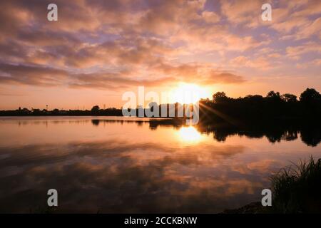 Symmetrie des Himmels in einem See bei Sonnenaufgang. Wolken spiegeln sich auf dem Wasser. Ruhige entspannende Szene mit einem schönen bunten Himmel und Sonnenstrahlen. Stockfoto