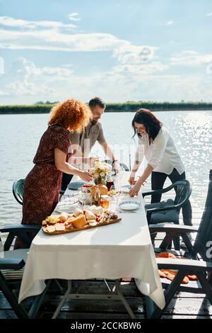 Freunde, die an einem See zu Abend essen und den Tisch legen Stockfoto