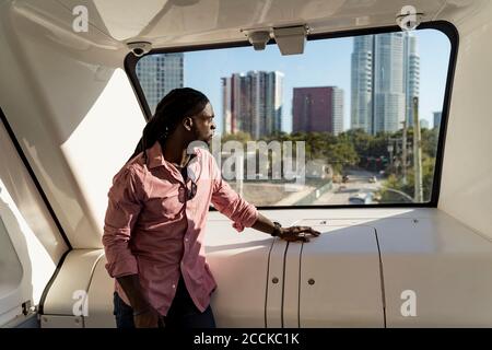 Junger Mann mit Dreadlocks, der durch das Fenster schaut, während er im Zug steht, Miami, Florida, USA Stockfoto