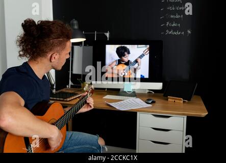 Mann, der Gitarre lernt, während er Tutorial zu Hause ansieht Stockfoto