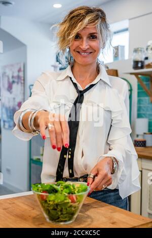 Lächelnde Köchin, die in der Kochschule Gewürze auf den Salat streut Stockfoto