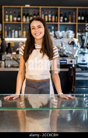 Glückliche weibliche Besitzerin, die an der Theke im Café steht Stockfoto