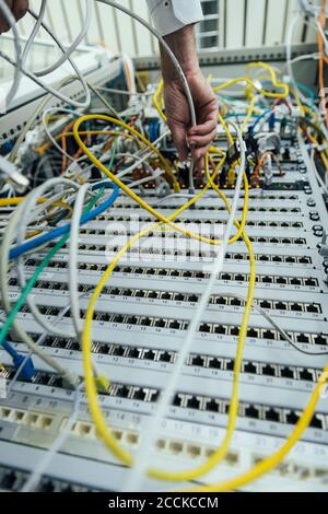 Anschlussfertiger Mann, der das Kabel am Rack des Rechenzentrums einsteckt Stockfoto