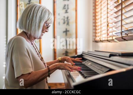 Lächelnde ältere Frau trägt Sonnenbrillen und spielt zu Hause Klavier Stockfoto