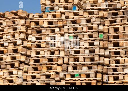 Gebrauchte Holzpaletten übereinander gestapelt entlang einer recycelten Holzwand zum Verladen und Transportieren von Waren. Eine Reihe von Plattformen für die Industrie Stockfoto