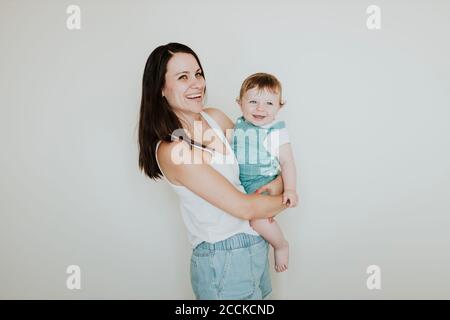 Glückliche Mutter trägt Baby Tochter, während an Wand stehen Zu Hause Stockfoto