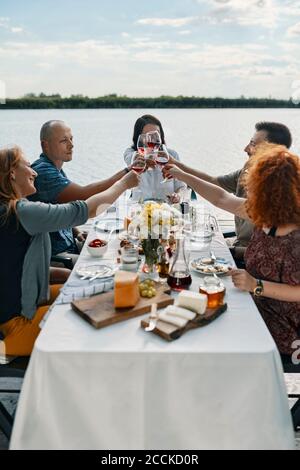 Freunde, die an einem See zu Abend essen, klirren Weingläser Stockfoto