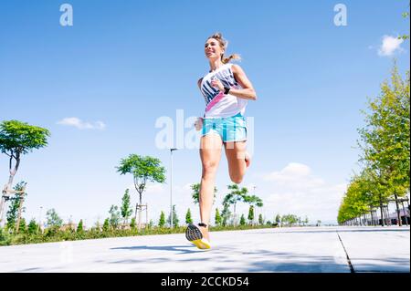 Mittlere Erwachsene Frau, die auf der Straße gegen den blauen Himmel joggt Stockfoto