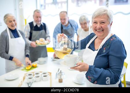 Ältere Frau gießt Tee in der Tasse für Kaffee Party in Altersheim Stockfoto