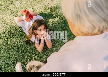 Nettes Mädchen mit Händen auf Kinn Blick auf Großmutter, während Liegen über grasbewachsenen Land im Hof Stockfoto