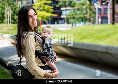 Lächelnde Mutter mit ihrem kleinen Jungen in Babytrage in Stadt Stockfoto