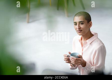 Porträt einer selbstbewussten Frau, die auf dem Boden sitzt Ein Loft mit einer Tasse Kaffee Stockfoto