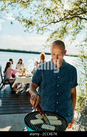 Mann grillen Halloumi Käse an einem See mit Freunden in Hintergrund Stockfoto