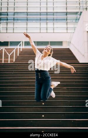 Junge Frau mit ausgestreckten Armen springen auf Treppe in der Stadt Stockfoto