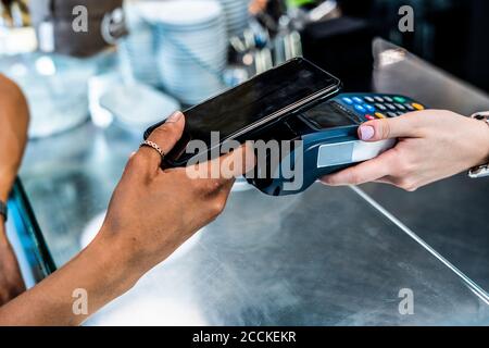 Weibliche Kundin, die kontaktlos über das Smartphone in Kaffee bezahlt Kaufen Stockfoto