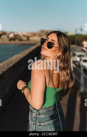 Junge Frau mit Sonnenbrille auf dem Weg gegen klaren Himmel stehen In der Stadt während des sonnigen Tages Stockfoto