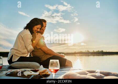 Pärchen beim Picknick am Steg an einem See bei Sonnenuntergang Stockfoto