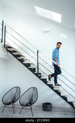 Mittelerwachsener Mann, der sich im modernen Penthouse die schwimmende Treppe hinunter bewegt Stockfoto