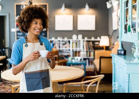 Nachdenkliche weibliche Besitzerin hält Kaffeetasse, während im modernen Stand Café Stockfoto