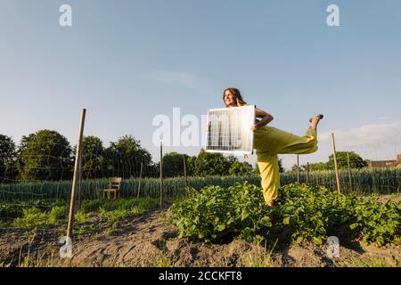 Junge Frau, die auf einem Gemüsefleck auf dem Land steht Solarpanel halten Stockfoto