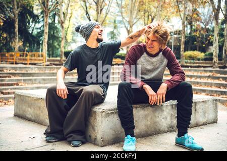 Lächelnd männlich aussehende Freunde Haare, während im öffentlichen Park sitzen Stockfoto