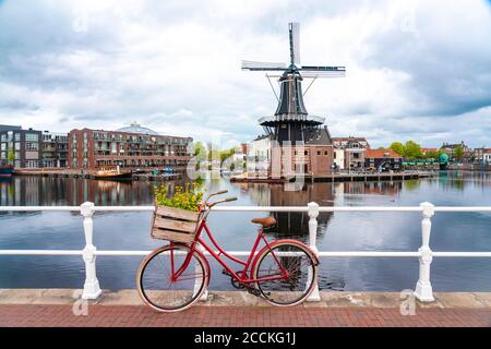 Niederlande, Nordholland, Haarlem, Fahrrad geparkt entlang Geländer der Kanalbrücke mit De Adriaan Windmühle im Hintergrund Stockfoto