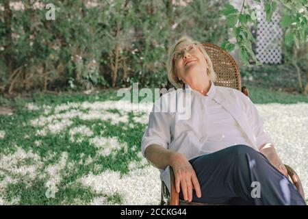 Nachdenkliche ältere Frau, die aufschaut, während sie sich auf einem Stuhl entspannt Hof Stockfoto