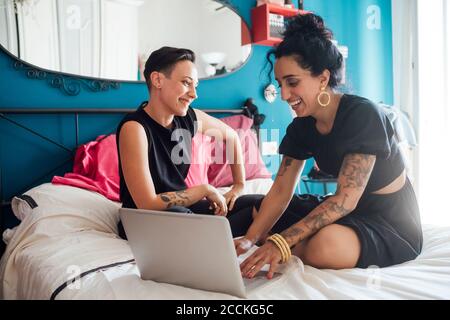 Lächelnde Frau, die den Partner mit einem Laptop im Schlafzimmer anschaut Stockfoto