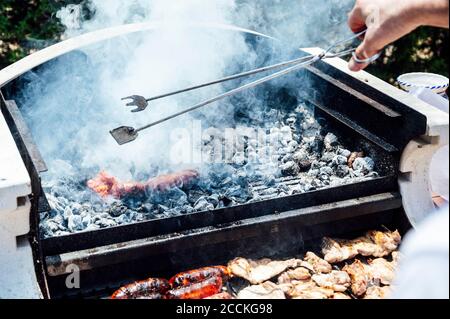 Hand des jungen Mannes, der die Servierzange über dem Grill hält Im Hof Stockfoto