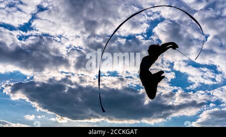 Junge Frau hält Band springen während Aerobic gegen bewölkt Himmel Stockfoto