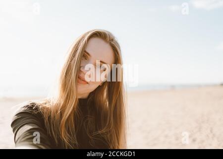 Hübsche Frau mit langen Haaren, blonde macht Selfie-Foto auf Handy. Schöne Frau mit Blick auf Kamera und kippbaren Kopf. Sandstrand an unny Tag im Meer oder Meer Küste Stockfoto
