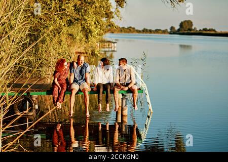 Freunde reflektierten sich im Wasser, das auf dem Steg an einem See saß Stockfoto