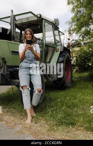 Junge Frau mit Handy an einem Traktor in der Auf dem Land Stockfoto
