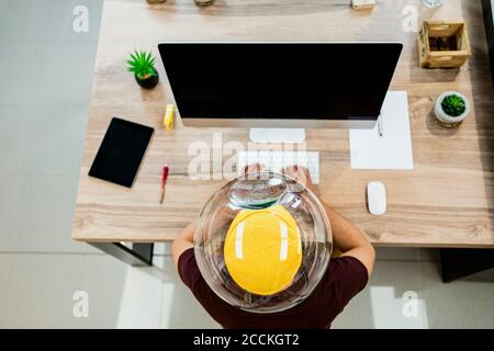 Geschäftsmann trägt Fischschüssel im Kopf, während mit Computer in modernen Büro Stockfoto