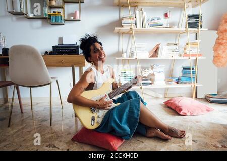 Frau spielt Gitarre im Wohnzimmer Stockfoto