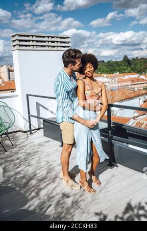 Romantisches multi-ethnisches Paar umarmt auf Penthouse Terrasse während sonnigen Tag Stockfoto